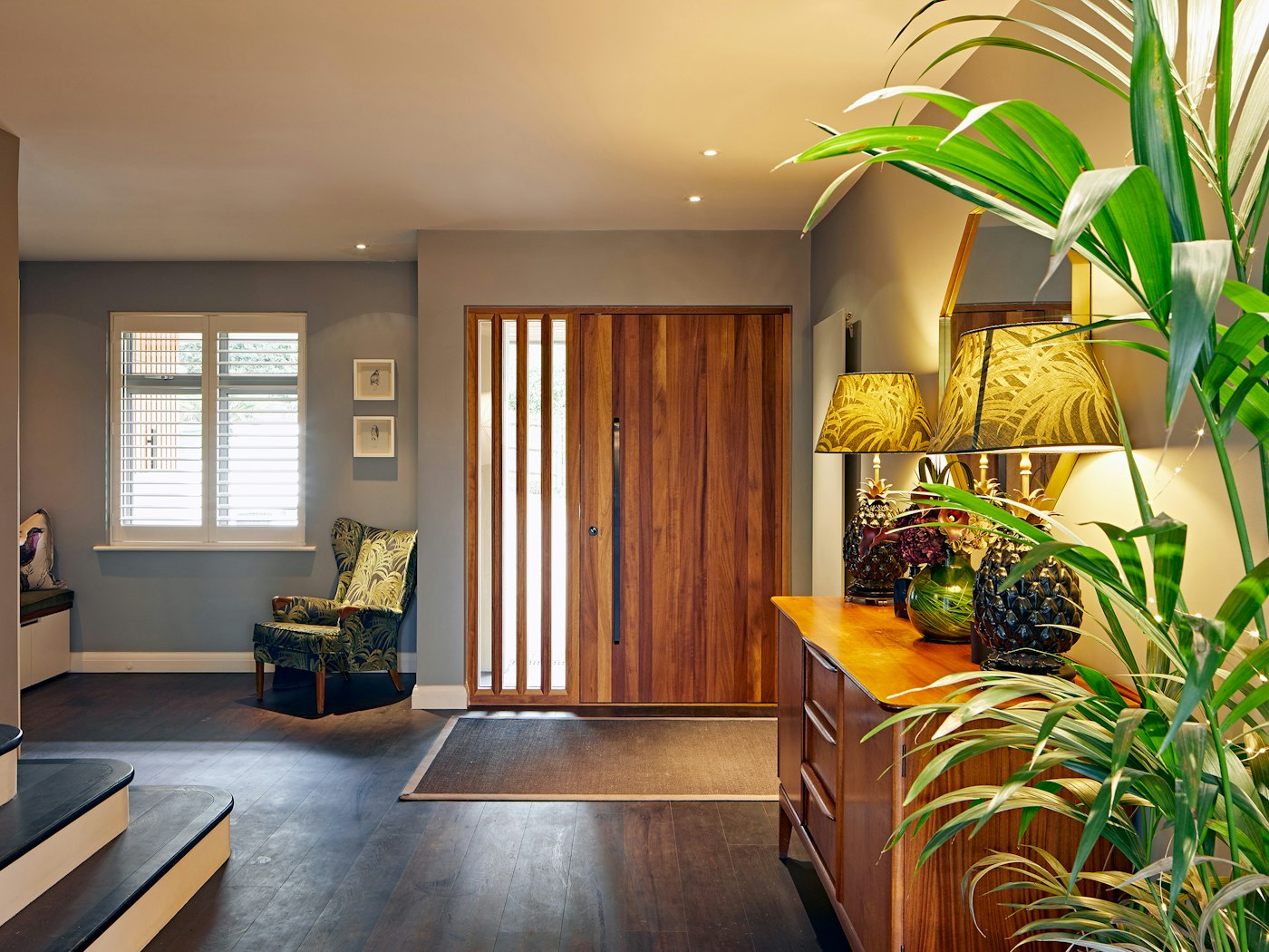 Fresh greenery and tropical-accented accessories give the hallway a burst of colour that lift the rich, dark flooring