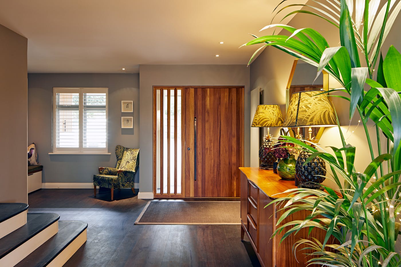 Fresh greenery and tropical-accented accessories give the hallway a burst of colour that lift the rich, dark flooring