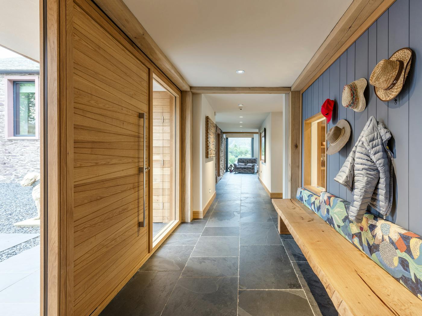 Warm wood, slate, and blue textured wall with hooks and seating creates a practical and attractive hallway