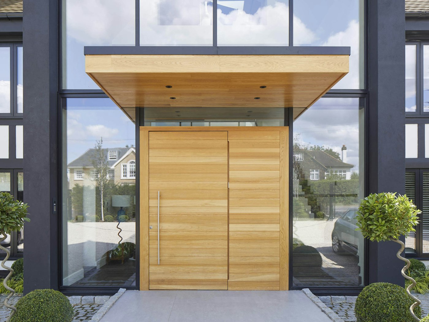 This metal & wooden front door canopy extends a long way in front of this pivot door to give shelter from sun & rain