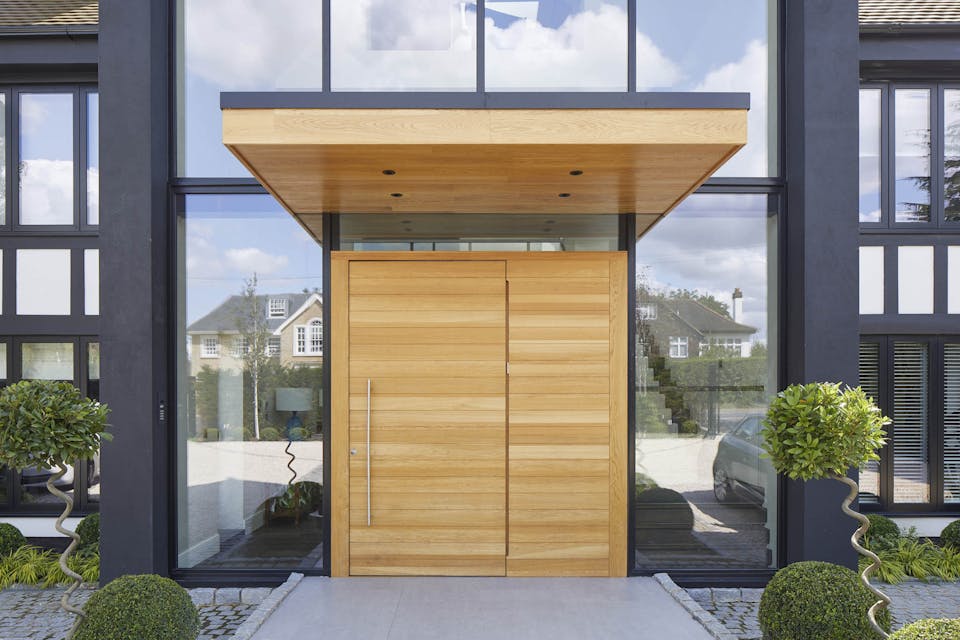 This metal & wooden front door canopy extends a long way in front of this pivot door to give shelter from sun & rain