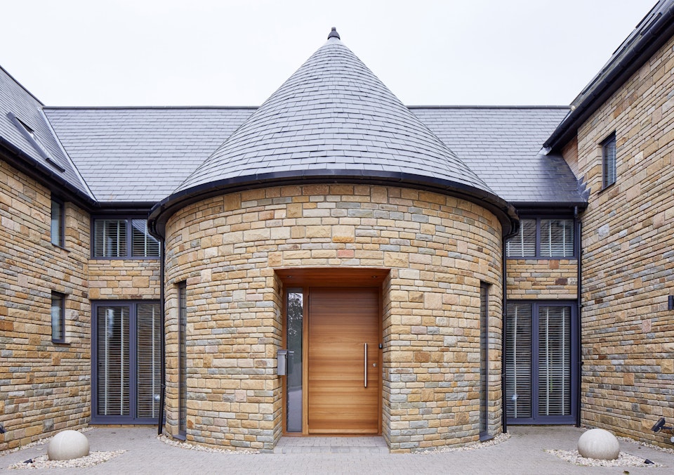 The iroko front door contrasts against the lighter stone in this house