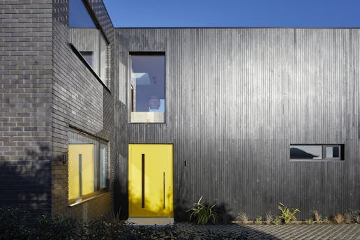 here a striking yellow door really makes a statement against the black cladding