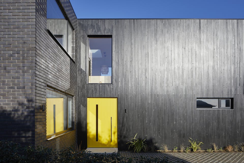 here a striking yellow door really makes a statement against the black cladding