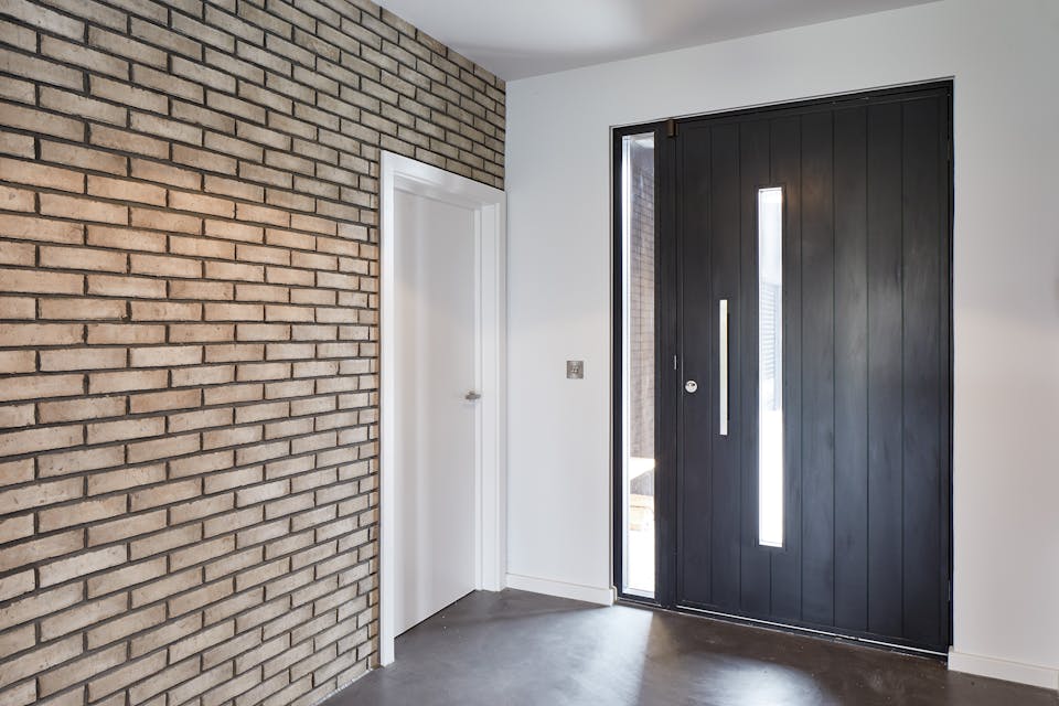 The brick wall & bright white paint nicely highlights the contemporary black door in this hallway