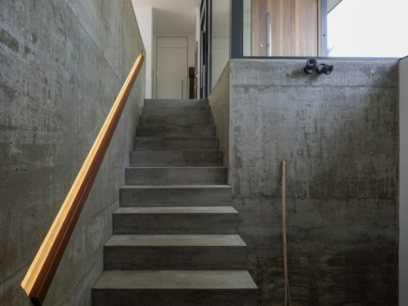 And from the bottom of the stairs, the concrete interior contrasts beautifully with the iroko front door seen through the glass