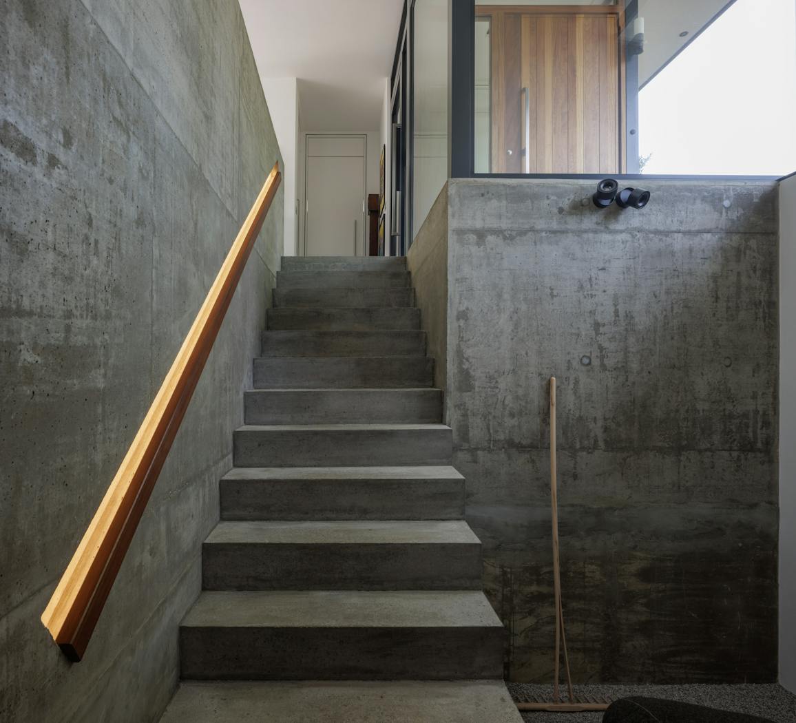 And from the bottom of the stairs, the concrete interior contrasts beautifully with the iroko front door seen through the glass