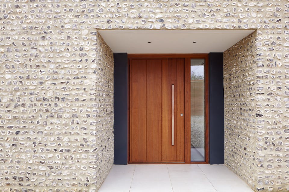 The iroko door is framed by dark grey & stone