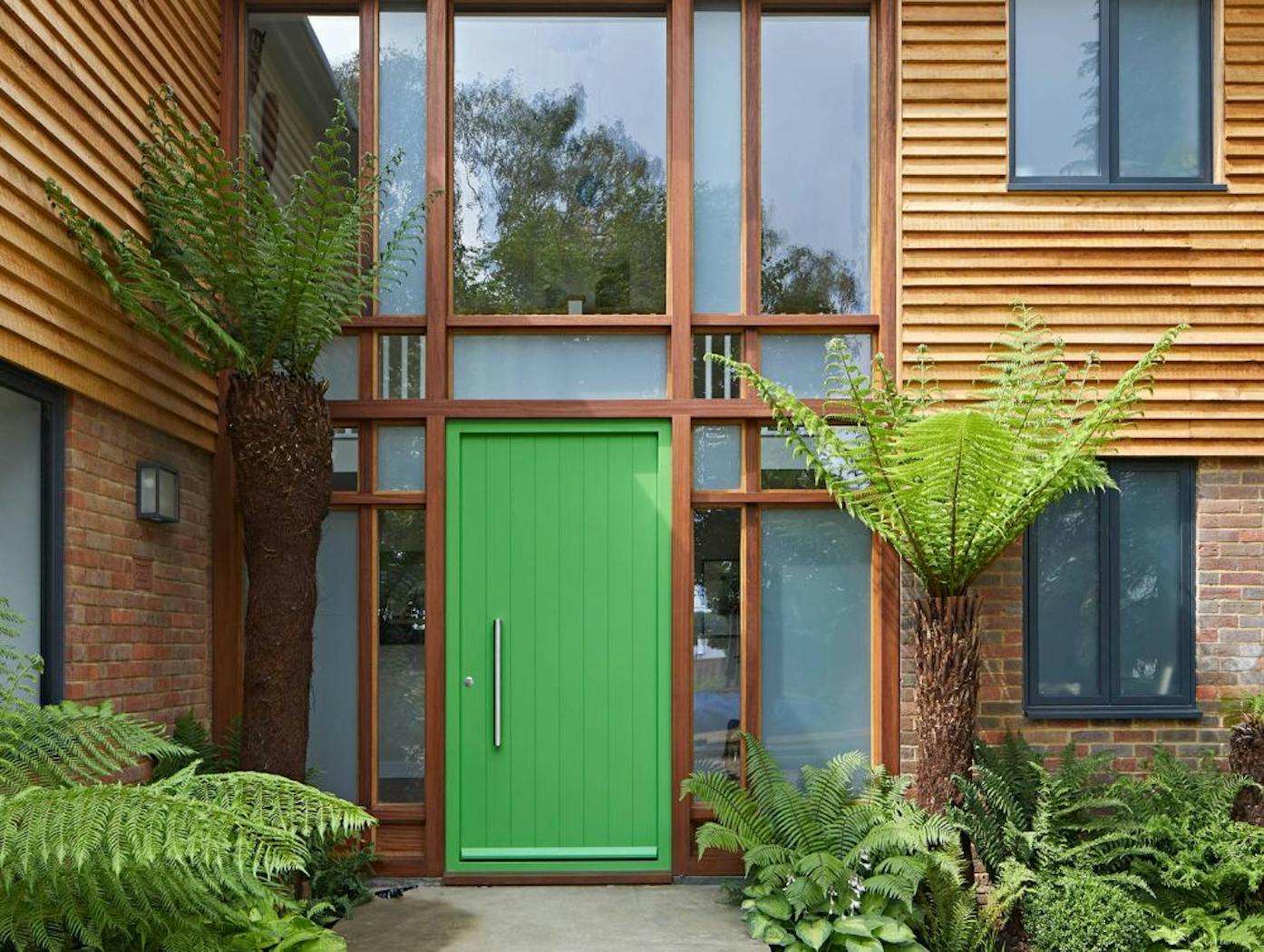 This green door looks amazing with wood cladding and tropical planting